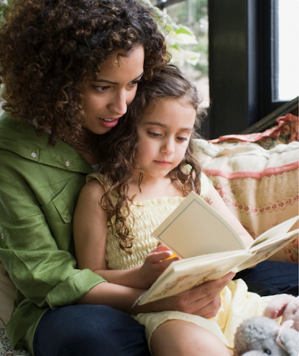 A woman holding her daughter in her lap and reading her a book 