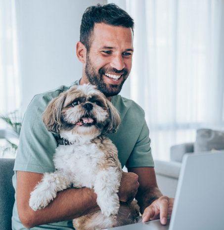 a man on his laptop smiling while holding his dog